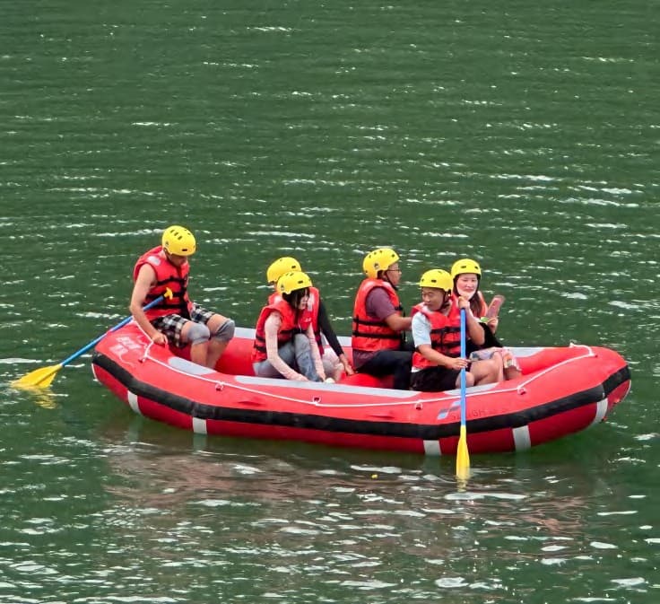 Five people in helmets and life jackets paddling a red inflatable on a lake